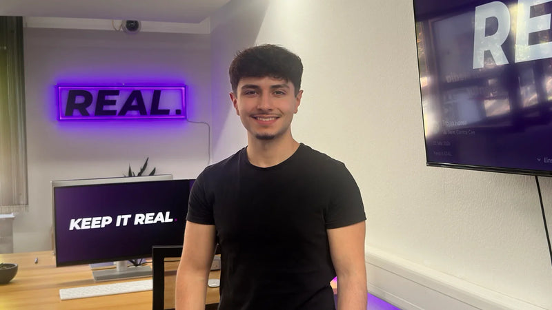 Emre Tuncer, Gründer der Social Media Agentur REAL., vor der lila REAL.-Leuchtschrift im Büro